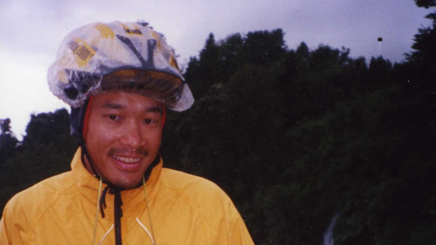 A cyclist in a yellow rain jacket and helmet outdoors.